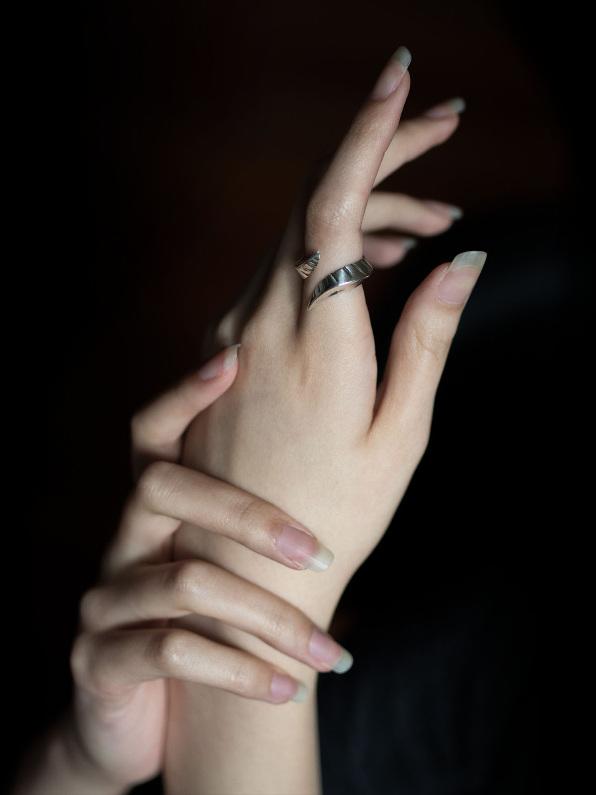 Aubrie's hands are posed delicately to feature a silver ring on her left index finger. The loop of the ring is broken by a split, and each end is a draconian prong pointing away from the other.